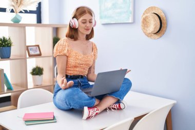 Young redhead woman sitting on table doing yoga exercise at home