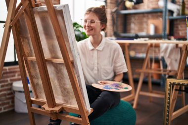 Sanat stüdyosunda kendine güvenen genç sarışın sanatçı gülümsüyor.