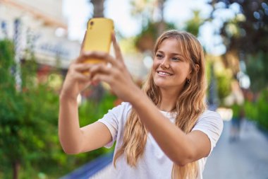 Parktaki akıllı telefonun yanında kendinden emin gülümseyen genç sarışın kız.