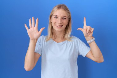 Kafkasyalı bir kadın günlük mavi tişört giyer ve yedinci parmaklarını göstererek gülümseyerek mutlu ve kendinden emin görünür.. 