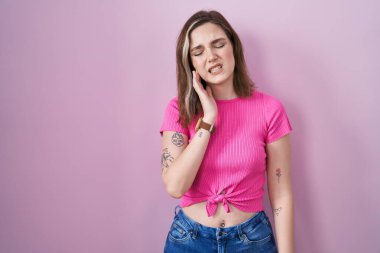 Blonde caucasian woman standing over pink background touching mouth with hand with painful expression because of toothache or dental illness on teeth. dentist 