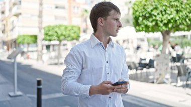 Young caucasian man using smartphone with serious expression at coffee shop terrace