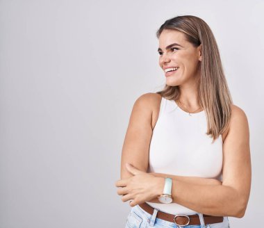 Beyaz arka planda duran İspanyol genç bir kadın yüzünde gülümseme, doğal bir ifade ile yan yana bakıyor. Kendinden emin gülen. 