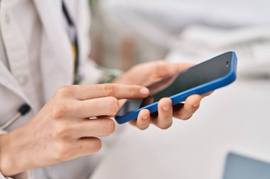 Genç beyaz kadın doktor klinikte çalışan akıllı telefonu kullanıyor.