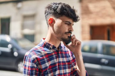 Young hispanic man talking on the smartphone at street