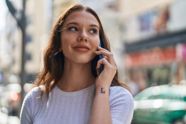 Gülümseyen genç bir kadın caddedeki akıllı telefondan konuşuyor.