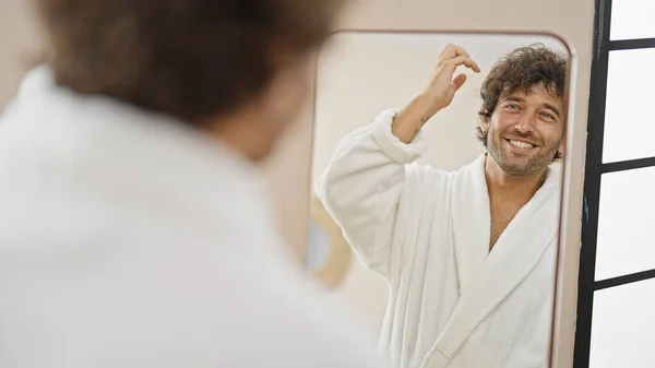Jovem Hispânico Vestindo Roupão Pentear Cabelo Com Mãos Olhando Espelho — Fotografia de Stock