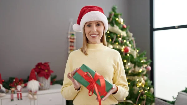 Νεαρή Ξανθιά Γυναίκα Κρατώντας Δώρο Στέκεται Δίπλα Στο Χριστουγεννιάτικο Δέντρο — Φωτογραφία Αρχείου