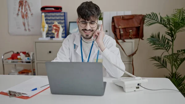 Mladý Hispánský Muž Lékař Pomocí Notebooku Mluvit Telefonu Klinice — Stock fotografie