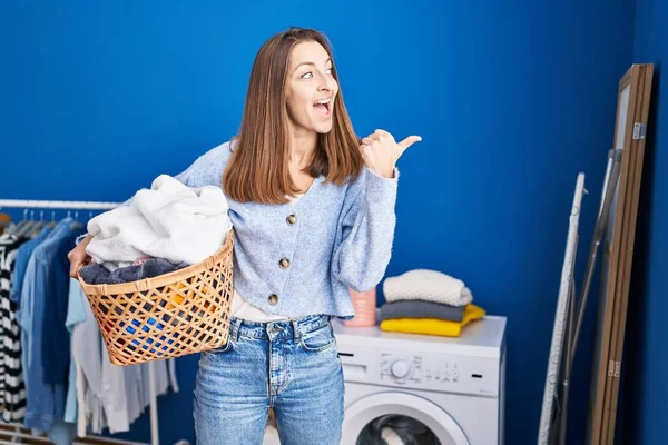 Ung Kvinna Håller Tvättkorg Pekar Tummen Upp Till Sidan Ler — Stockfoto