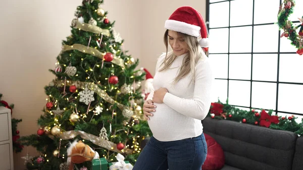 若いです妊娠中の女性身に着けていますクリスマス帽子タッチ腹ホーム — ストック写真