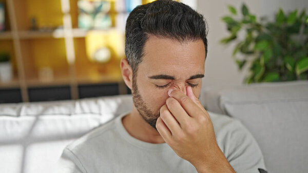 Young hispanic man crying sitting on the sofa at home