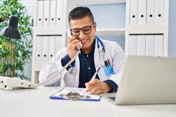 Νεαρός Λατίνος Γιατρός Μιλάει Στο Τηλέφωνο Γράφοντας Έγγραφο Στην Κλινική — Φωτογραφία Αρχείου