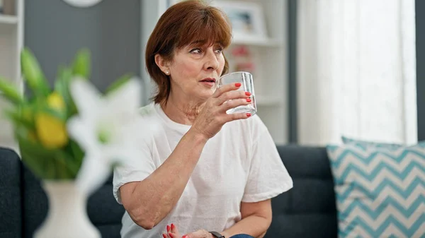 Kobieta Średnim Wieku Pije Szklankę Wody Siedząc Kanapie Domu — Zdjęcie stockowe