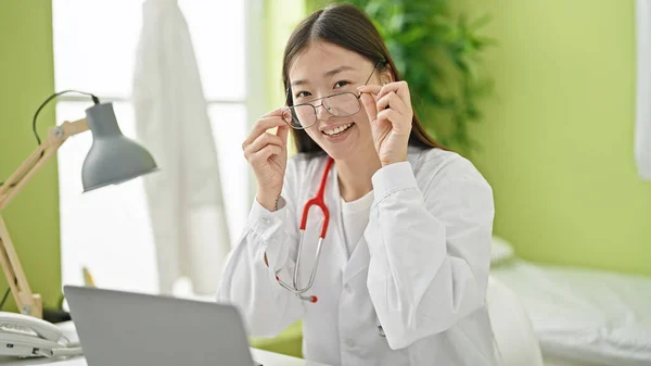 若いです中国人女性医師使用ラップトップ着用眼鏡でクリニック — ストック写真