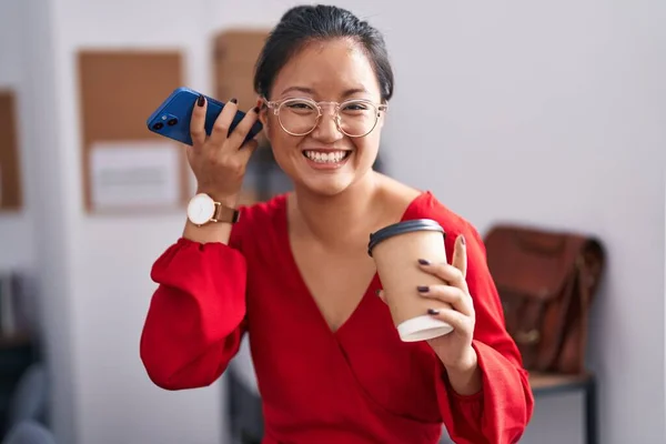 若い中国人女性ビジネスマンがオフィスでコーヒーを飲むスマートフォンの音声メッセージを聞く — ストック写真