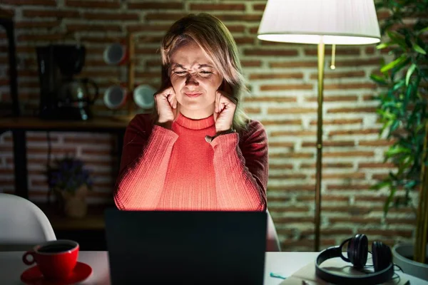 Blond Kvinna Använder Laptop Natten Hemma Täcker Öronen Med Fingrar — Stockfoto