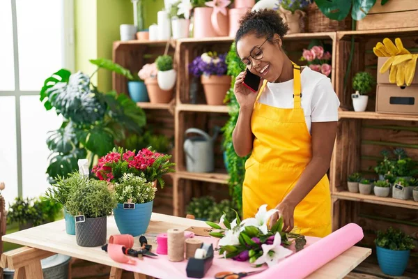 Afro-Amerikan kadın çiçekçi gülümsüyor çiçekçide akıllı telefondan konuşuyor.