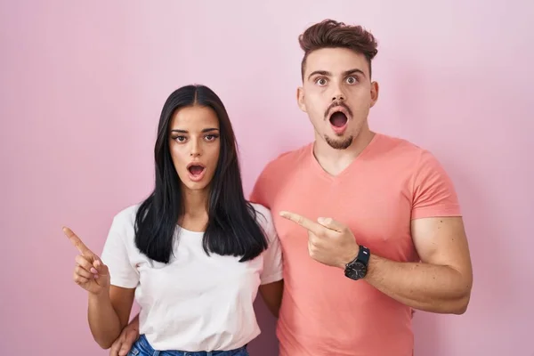 Jong Hispanic Paar Staande Roze Achtergrond Verrast Wijzend Met Vinger — Stockfoto