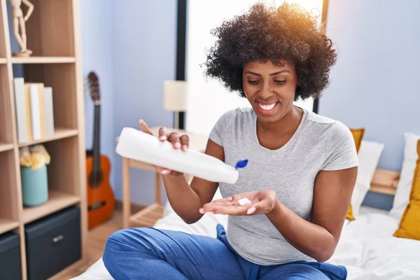 stock image African american woman pouring lotion on hand sitting on bed at bedroom