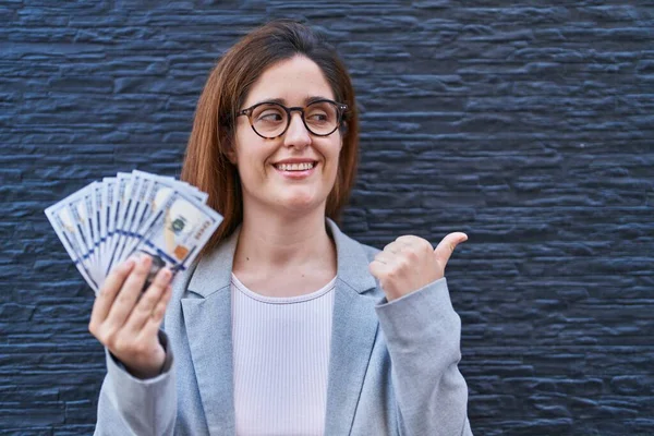 Morena Mulher Segurando Dólares Apontando Polegar Até Lado Sorrindo Feliz — Fotografia de Stock