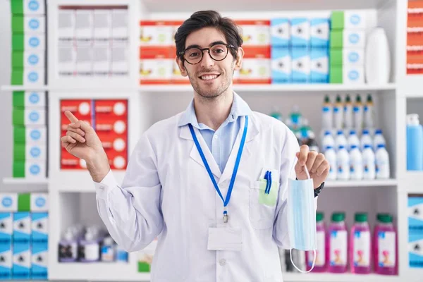 Νεαρός Ισπανός Που Εργάζεται Στο Φαρμακείο Κρατώντας Μάσκα Ασφαλείας Χαμογελώντας — Φωτογραφία Αρχείου