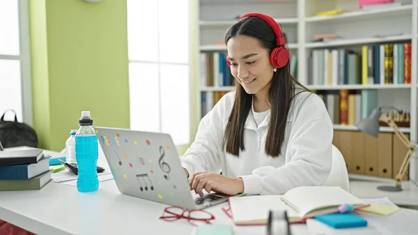 大学の教室で勉強するラップトップとヘッドフォンを使用して若い美しいヒスパニック系女性の学生 — ストック写真