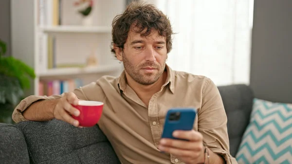 自宅でスマートフォンのコーヒーを使用して若いヒスパニック系男性 — ストック写真