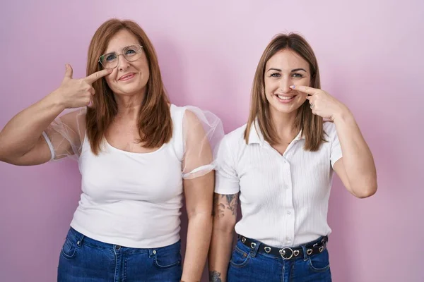 西班牙裔母亲和女儿穿着宽松的白色T恤 背景是粉色的 手指头对着鼻子 美的概念 — 图库照片