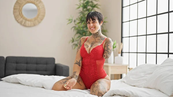 Hispanic woman with amputee arm wearing lingerie sitting on bed smiling at bedroom