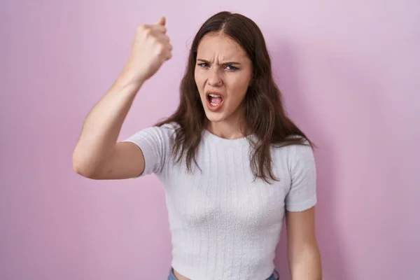 ピンク色の背景に立っている若いヒスパニック系の女の子は怒りで叫んでいる間 怒りと怒りの拳を上げる怒っています 怒りと攻撃的な考え方 — ストック写真
