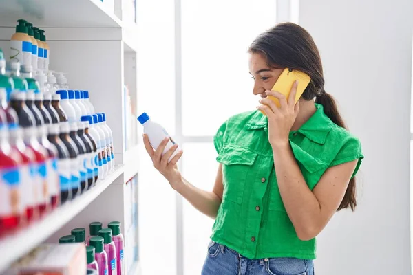他惊慌失措的年轻女性顾客在药店拿着药瓶用智能手机交谈 — 图库照片
