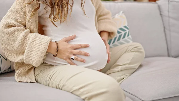 若いです妊娠中の女性座っています上のソファマッサージ腹ホーム — ストック写真