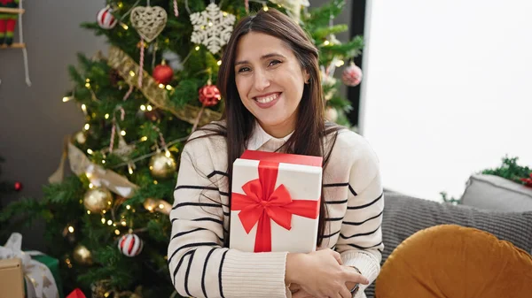Νεαρή Όμορφη Ισπανόφωνη Γυναίκα Κρατώντας Χριστουγεννιάτικο Δώρο Χαμογελώντας Στο Σπίτι — Φωτογραφία Αρχείου