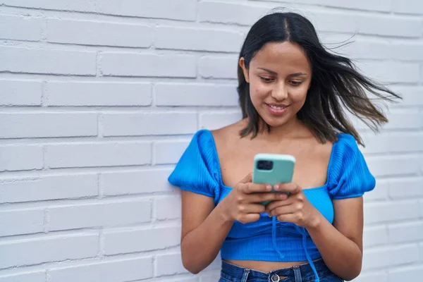 若いですヒスパニック女性笑顔自信を持って使用してスマートフォン上の白い隔離されたレンガの背景 — ストック写真