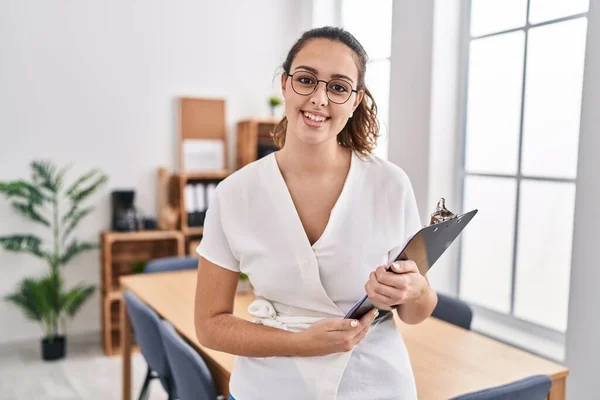 stock image Young beautiful hispanic woman business worker smiling confident holding clipboard at office