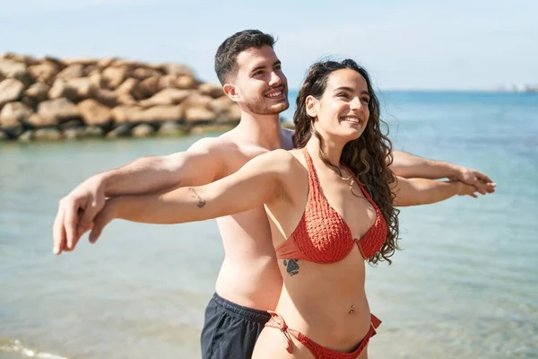 Young Hispanic Couple Tourists Wearing Swimsuit Standing Arms Open Seaside — Stok fotoğraf