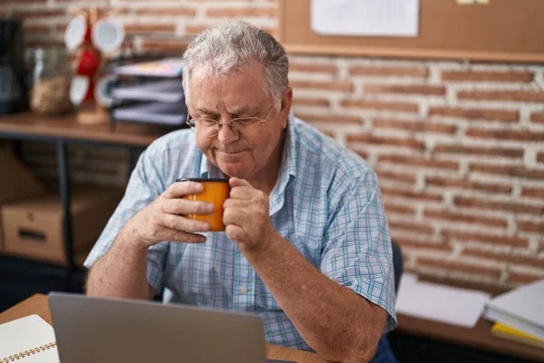 中年白发苍苍的生意人在办公室用笔记本电脑喝咖啡 — 图库照片