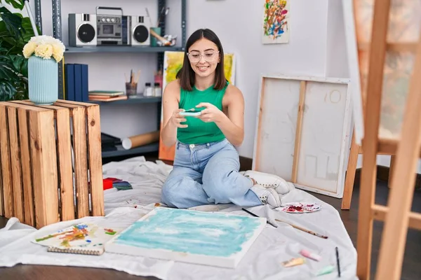 若いヒスパニック系の女性アーティストがアートスタジオでスマートフォンで写真を撮る — ストック写真