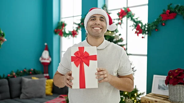 Νεαρός Ισπανός Άνδρας Χαμογελά Σίγουρος Κρατώντας Χριστουγεννιάτικο Δώρο Στο Σπίτι — Φωτογραφία Αρχείου