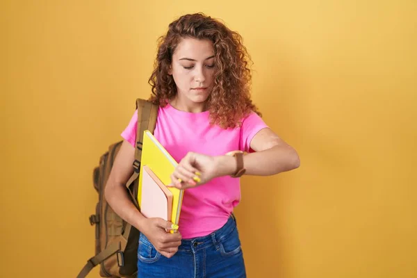年轻的高加索女人 背着学生背包 拿着书本 用腕表检查时间 放松而自信 — 图库照片