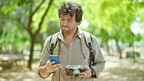 公園でヴィンテージカメラを持っているスマートフォンを使用して若いヒスパニック系の男の観光客 — ストック写真