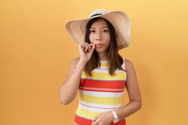 黄色の背景の口と唇の上に夏の帽子を身に着けている中国の女性は指でジップとしてシャットダウンします 秘密裏に黙ってタブーを語る — ストック写真