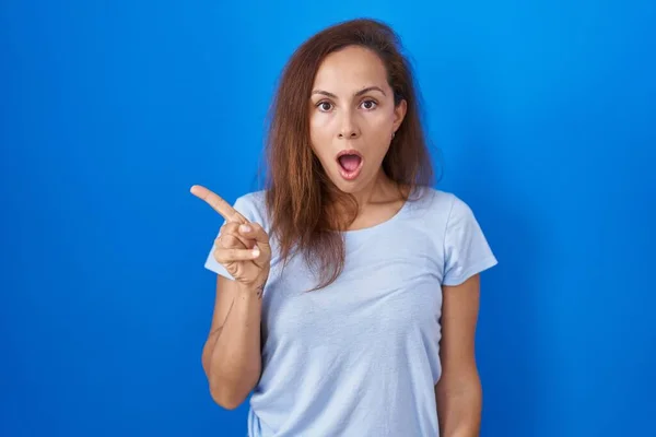 Mujer Morena Pie Sobre Fondo Azul Sorprendida Señalando Con Dedo —  Fotos de Stock