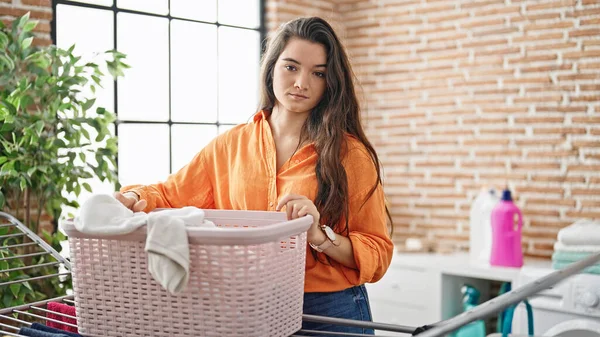 若い美しいヒスパニック系の女性が洗濯室で服でバスケットを保持 — ストック写真