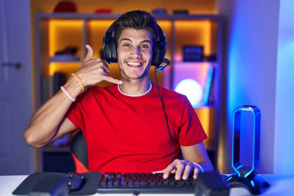 Молодой Латиноамериканец Играющий Видеоигры Улыбаясь Делает Телефонный Жест Рукой Пальцами — стоковое фото