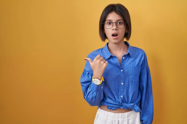 Junges Mädchen Steht Über Gelbem Hintergrund Überrascht Und Zeigt Mit — Stockfoto