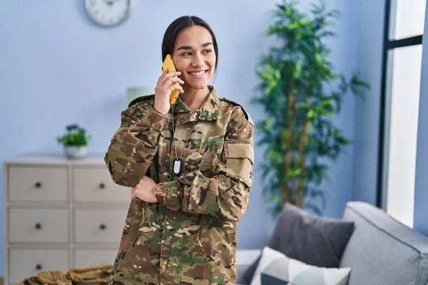 Young hispanic woman army soldier talking on the smartphone at home