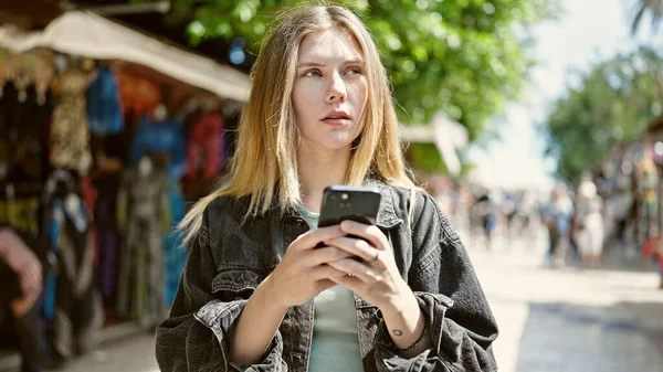 ストリート市場で深刻な顔を持つスマートフォンを使用して若いブロンドの女性 — ストック写真