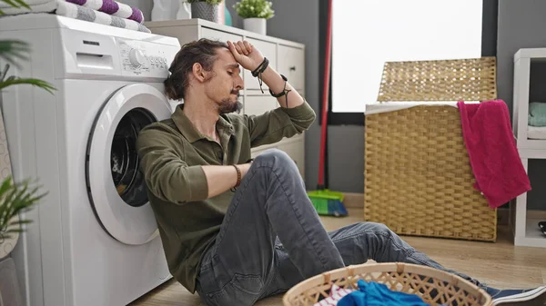 年轻的惊慌失措的男人坐在洗衣房的地板上洗衣服 — 图库照片